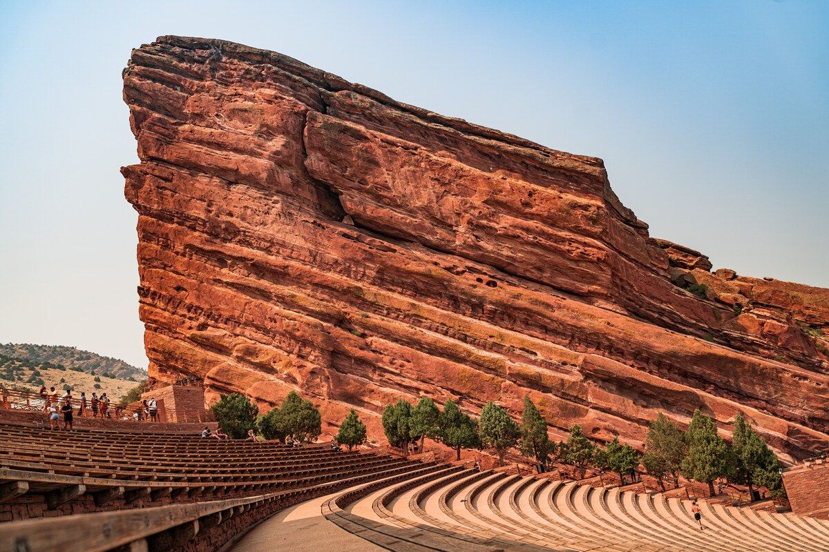 A towering red sandstone monolith with horizontal strata above the curved bench rows of Red Rocks Amphitheatre near Denver.