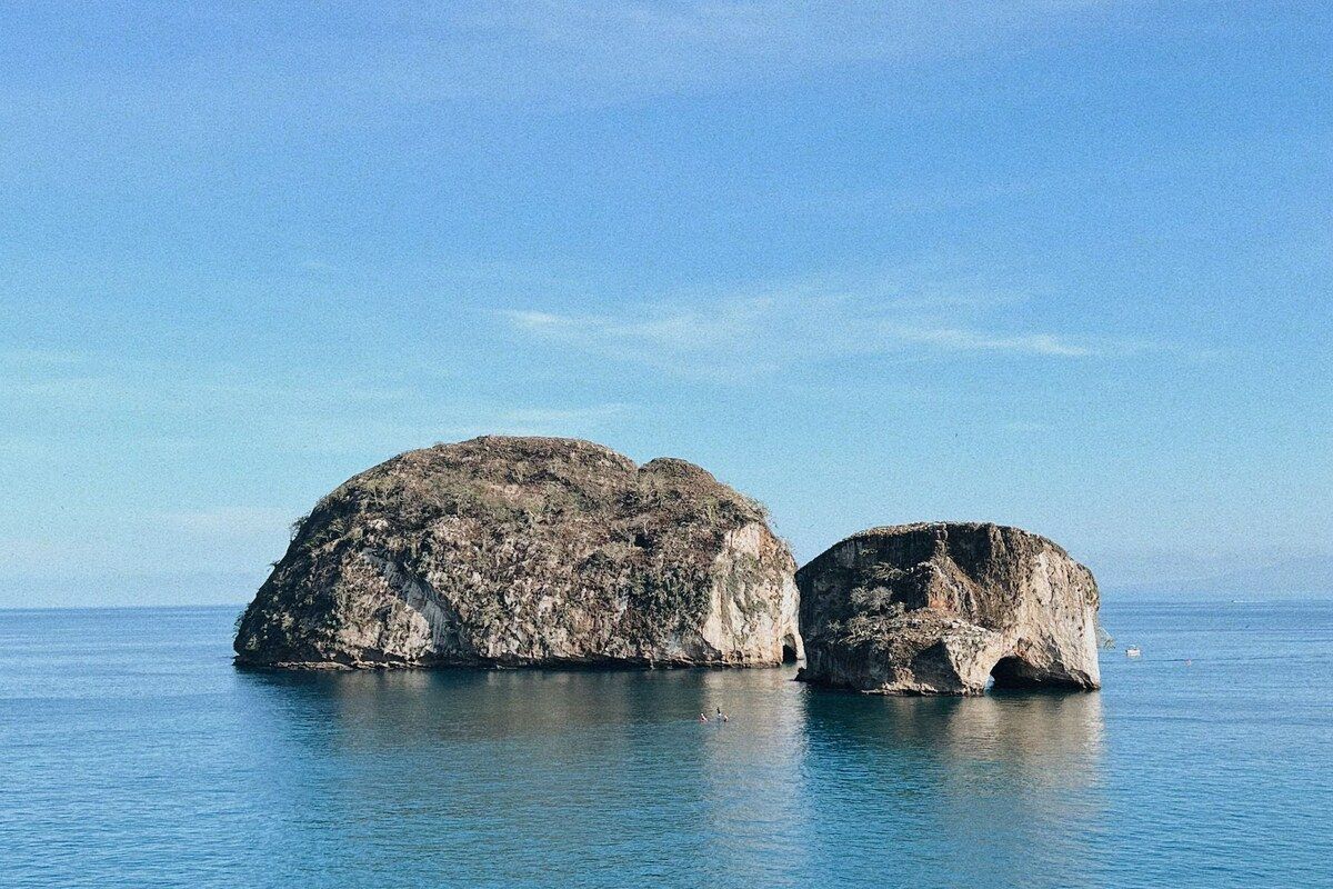 The Los Arcos sea stacks and their rock arch standing in calm blue water on the coast south of Puerto Vallarta.