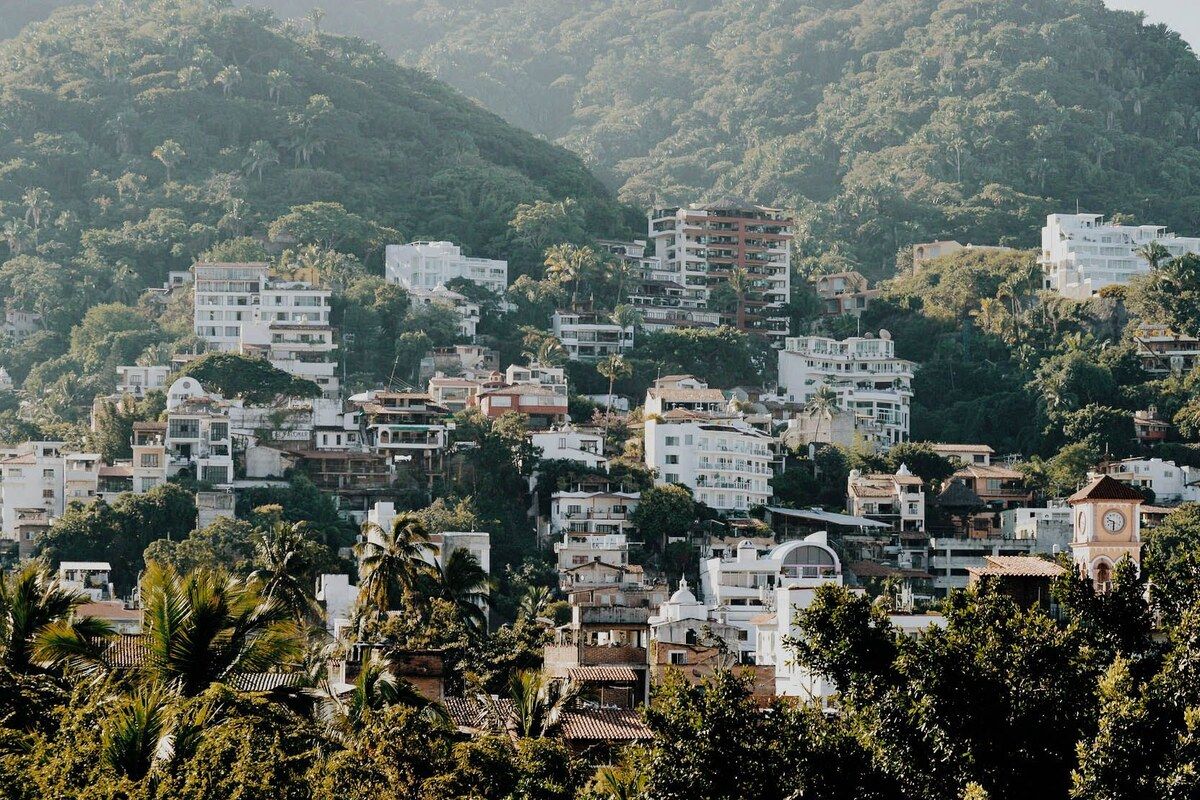 White and terracotta houses stacked up a jungle hillside above Puerto Vallarta, a small clock tower among the rooftops.