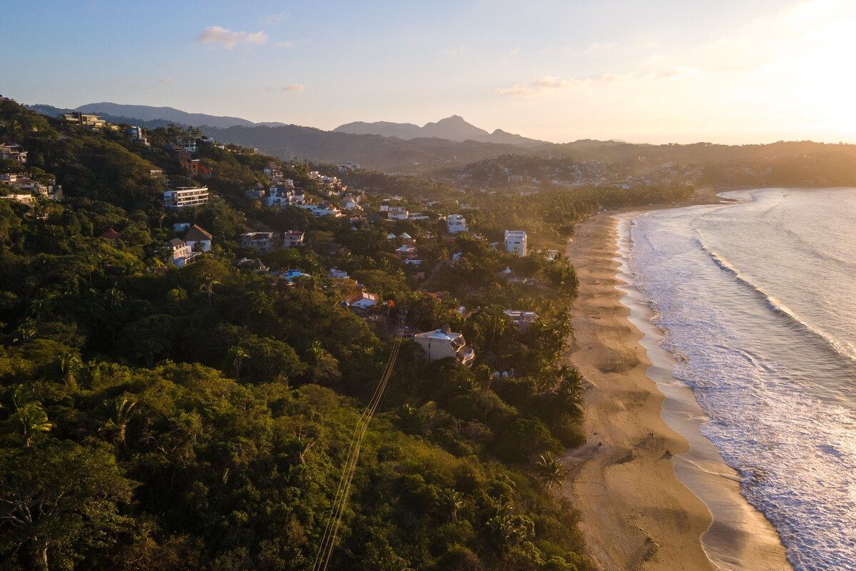 Sunset over the surf beach at Sayulita north of Puerto Vallarta, waves breaking along the sand below a jungle hillside.